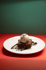 Brownie topped with ice cream scoop and chocolate drizzle, plated.