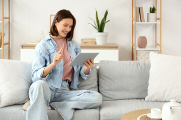 Obraz premium Young woman using tablet computer on sofa at home