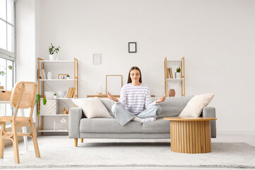 Young woman meditating on sofa at home