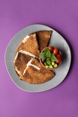 Lebanese grilled cheese markouk with fresh vegetables on purple background.