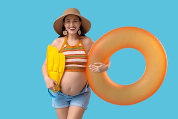 Young pregnant woman with inflatable ring and flippers on blue background. Traveling concept