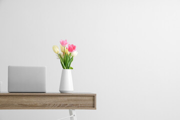 Stylish workspace with modern laptop and beautiful flowers near white wall