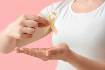 Young woman with yellow ribbon on pink background, closeup. Cancer awareness concept