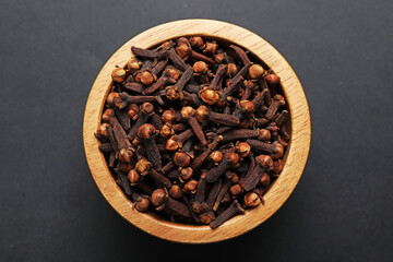 Aromatic cloves in bowl on dark table, top view