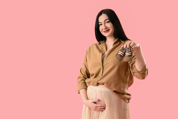 Beautiful pregnant woman with baby booties on pink background