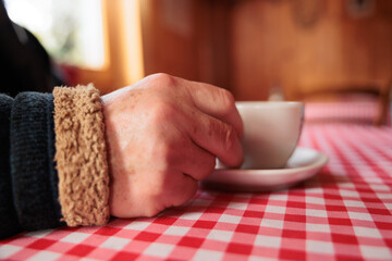 dettagli di una mano di un uomo adulto, in abiti invernali, seduto ad un tavolo di un bar di montagna, mentre tiene una tazza di caffè