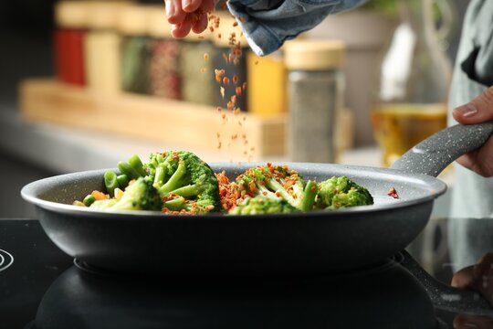 Woman adding spices to dish in kitchen, closeup