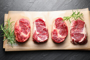 Pieces of raw beef meat, rosemary and salt on black table, top view