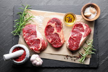 Pieces of raw beef meat and spices on black table, flat lay
