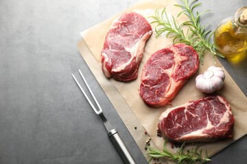Pieces of raw beef meat, spices and carving fork on grey table, flat lay. Space for text