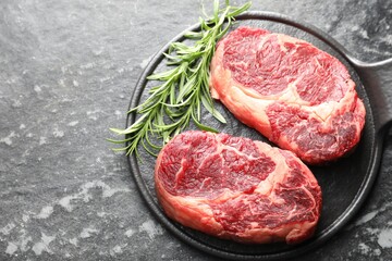 Pieces of raw beef meat and rosemary on dark table, top view. Space for text