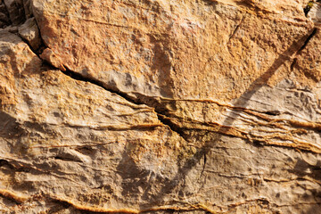vista macro di una parete rocciosa naturale dalle sfumature di colore marrone e arancione chiaro, con venature in rilievo e piccole fratture