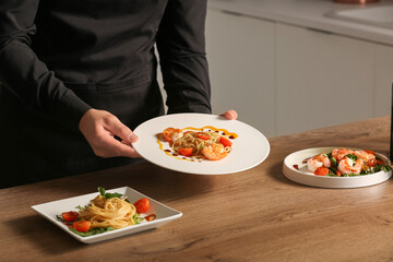 Male chef and tasty pasta with shrimps on table in kitchen, closeup