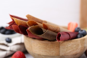 Tasty fruit leather rolls and berries on white table, closeup
