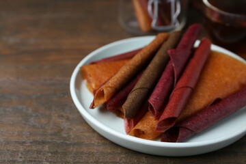 Tasty fruit leather rolls on wooden table, closeup. Space for text