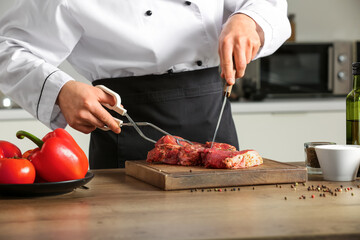 Male chef cutting raw meat at table in kitchen, closeup