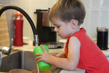 portrait of cute toddler boy washing dishes in the kitchen sink	