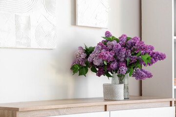Vase with beautiful lilac flowers on chest of drawers in living room