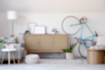Blurred view of light living room with bicycle, commode and lamp