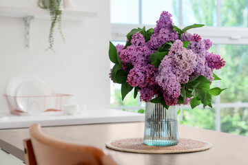 Vase with lilac flowers on table in kitchen