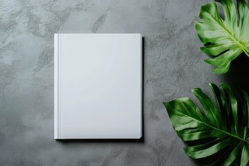Blank white book on gray textured surface with tropical leaves