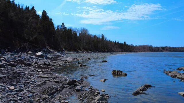 Flying over a rocky beach on the shore of a saltwater bay, rising above the surrounding forest. St. Lawrence River, Quebec, Canada, 2025.