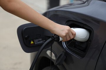 Woman hand puts the car on EV charging. Electric car Electric car charging in urban parking lot at...
