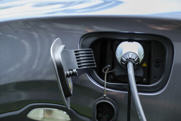 Electric car charging in urban parking lot at day, focus on EV charger station cable plugged into...