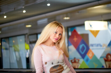 A blonde in a pink sweater and blue jeans poses for a photo. She smiles and she is happy. She has a beautiful figure.