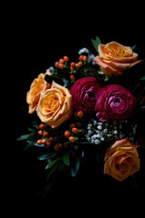 A beautifully arranged bouquet with orange roses and other flowers, against a black background.