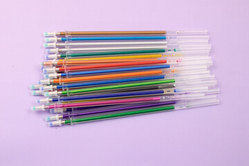 Multicolored ballpoint pens and ink refills on purple background stationery