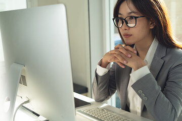 Asian business woman working on desktop computer, looking the screen, thinking about business prolect planning at office. Thoughtful businesswoman concentrate on  work