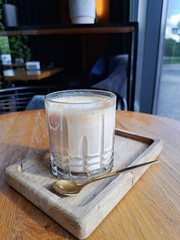 Aromatic cappuccino in a glass on a wooden stand in the interior of a cafe.