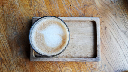 Aromatic cappuccino in a glass on a wooden stand in the interior of a cafe.