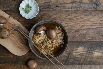 Hot noodle soup with mushrooms and thyme on a wooden table with cutting board and chopsticks