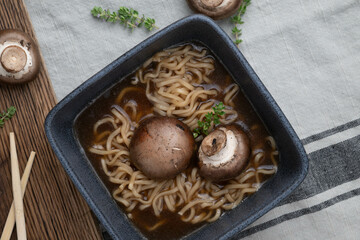 Close-up view from above, mushroom and noodle soup in a black square bowl on a marbled background.