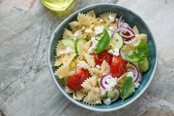 Green bowl with farfalle pasta salad on a grey granite background, horizontal shot, high angle view