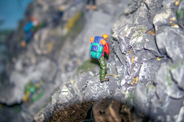 Miniature mountain climber figure scaling a rocky cliff with a colorful backpack