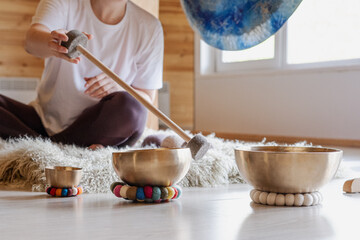 Seated individual using singing bowls for meditation. The focus is on creating calming sounds with the bowls. The scene depicts a peaceful setting on a soft rug