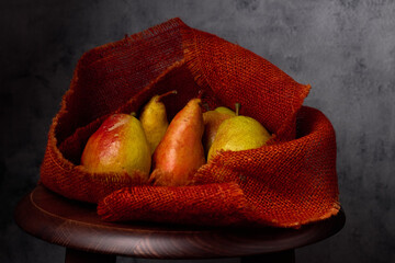 Fresh pears wrapped in rustic red burlap on a wooden stool with texture