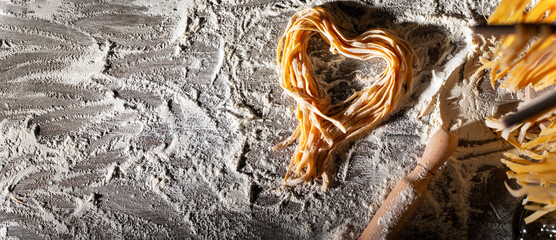 Heart shaped noodles on floured kitchen table top view cooking background with copy-space