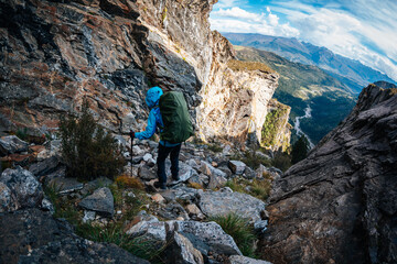 Backpacking woman climbing up on steep cliff edge at high altitude mountains top