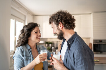 Happy couple drinking milk in kitchen and smiling at each other