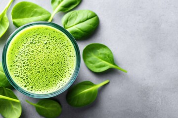 Green spinach smoothie in glass surrounded by fresh leaves on neutral surface