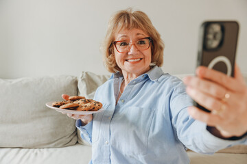 Senior woman taking selfie while showing plate of chocolate chip cookies