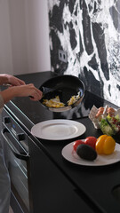 Beautiful young woman cooking vegetable scramble for breakfast in her kitchen early in the morning