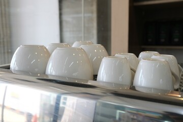 Neatly stacked white ceramic coffee cups placed upside down on a metallic espresso machine in a modern café, ready for serving hot beverages.