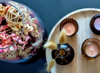 Close-up of a wooden tray with lit candles and a small vase with dried grasses, next to a glass...