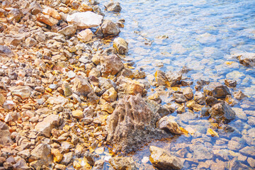 Rocky shoreline with various sizes and shapes of stones extending into clear, shallow water. Dry rocks on the shore and the submerged stones in water highlights the transition between land and sea