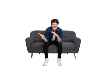 Full body image of young Asian man using phone sitting on sofa on PNG background	